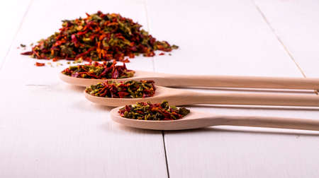 three wooden spoons  with dried peppers and seeds (chili peppers, habanero, jalapeno, rawit, birds eye chili, thai chili) on a white wooden place.の写真素材