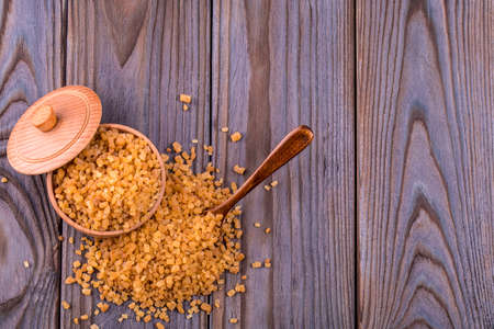 Wooden scoop spoon and bowl full of brown cane sugar with pinch of sugar spilled around on wooden table, top viewの写真素材