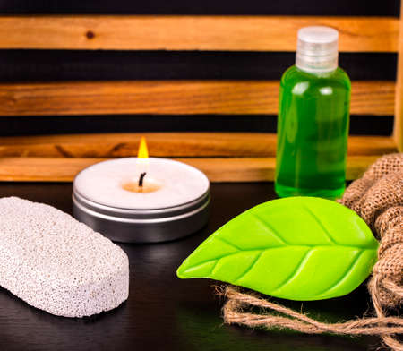 Composition of spa treatment on wooden background. Soap, candle, bottle of oil, pumice and burlap on black table.の写真素材