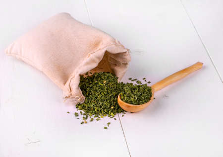 bag with dried green spices and a wooden spoon on a white kitchen table
