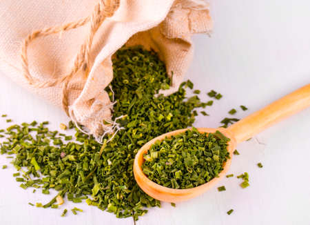 Baggy sack with dried green spices and a wooden spoon on a white kitchen tableの写真素材