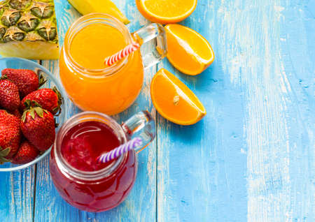 Fresh pineapple and strawberry smoothie in glasses with fruits on a blue wooden rustic background. Freshly blended summer drink nice to drink during a hot day.の写真素材