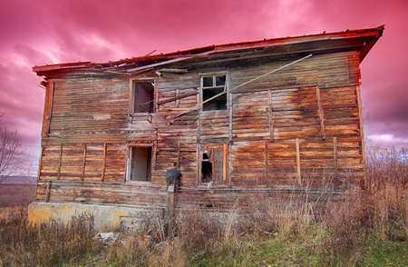 old ugly dilapidated wooden house on a background of red sky at sunsetの写真素材
