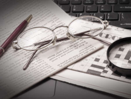 glasses and old newspaper lying on the black open laptop