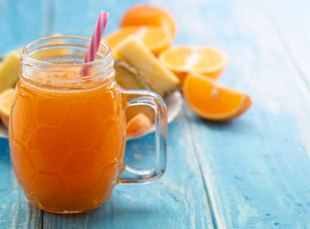 glass vessel with the juice of orange with a straw on a blue tableの写真素材