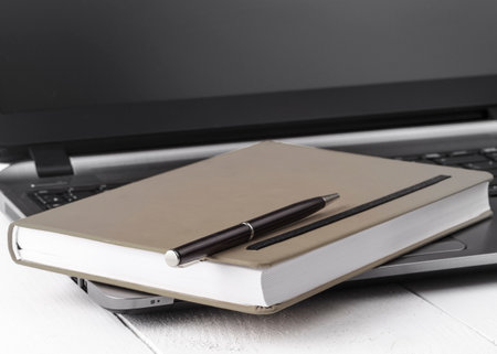 Orange notebook with a pencil lying on a laptopの写真素材