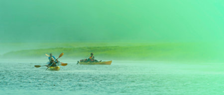 few people on kayaks travel across the lake in a misty morningの写真素材