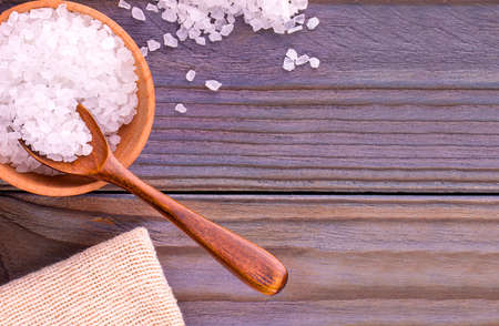 The white sea salt on cup, spoon and burlap on a wooden table