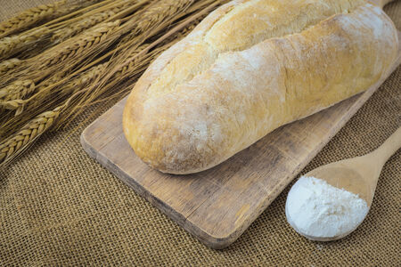 Bread on Bread Board with Wheat and Flour filled Spoon on Burlap Backgroundの写真素材