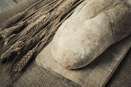 Bread on Bread Board with Wheat on Burlap Backgroundの写真素材