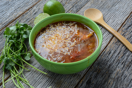 Tortilla Soup with Cheese, Lime, Cilantro and Wooden Spoon on Rustic Wood Backgroundの写真素材