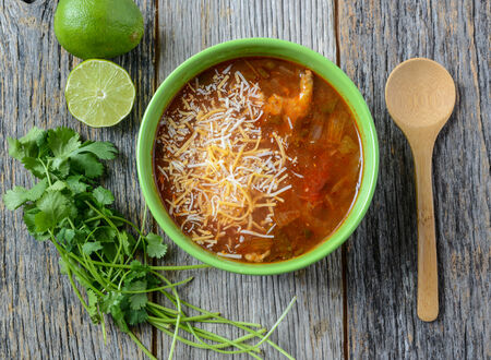 Tortilla Soup with Cheese, Lime, Cilantro and Wooden Spoon on Rustic Wood Backgroundの写真素材