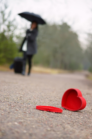 Heart on the road and woman with luggage and umbrellaの写真素材
