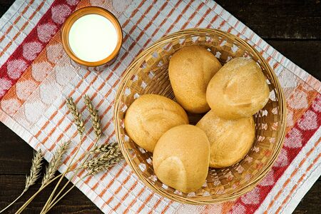 Fresh buns in wicker basket and milk cup on the tableclothの写真素材