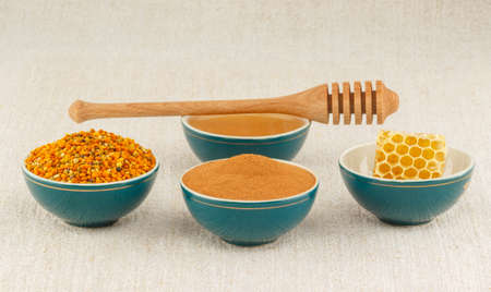 Pollen granules, honeycomb, honey and cinnamon in green porcelain bowls with wooden dipper, on rustic table clothの写真素材