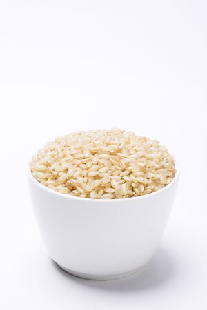 White Bowl Filled with Uncooked Brown Rice, Isolated on Whiteの写真素材