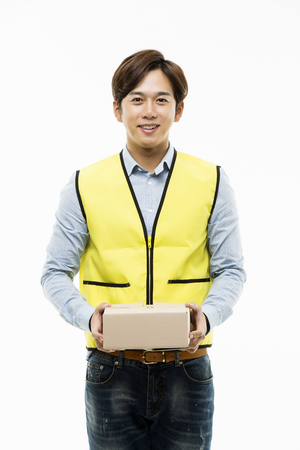Young Asian Man in a Yellow Vest Giving a Cardboard Boxの写真素材