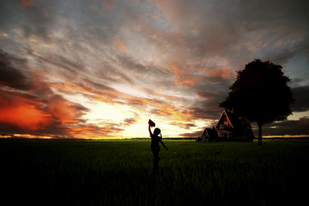 Silhouette of a little girl flying a paper airplane in the sunsetの写真素材