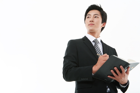 Young Asian businessman holding a notebook and a pen - isolated on whiteの写真素材