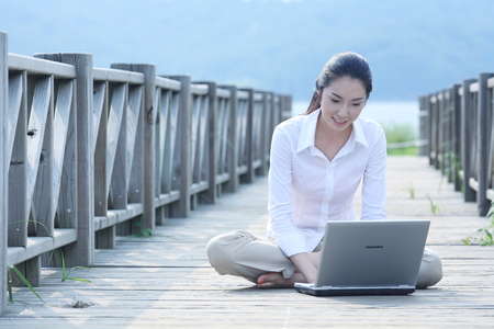 Young Asian woman working on her laptop on the wooden bridgeのeditorial素材