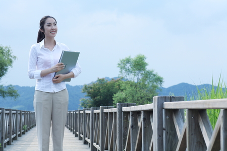 Young Asian woman holding a laptop on the wooden bridgeのeditorial素材