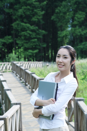 Young Asian woman holding a laptop on the wooden bridgeのeditorial素材