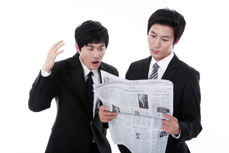 Two young Asian businessmen reading newspaper together - isolated on whiteのeditorial素材