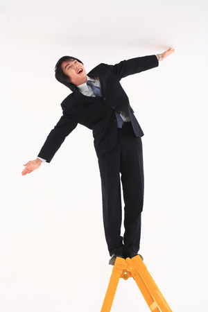 Asian businessman posing with a yellow ladder in the studio - isolated on whiteの写真素材