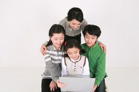 A female teacher and three kids looking at a laptop computer - isolated on whiteの写真素材