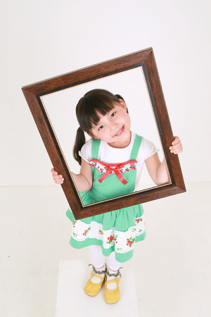Little Asian girl holding up a photo frame - isolated on whiteの写真素材