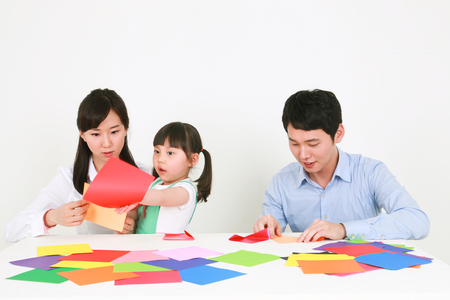 Adults and a little girl folding colored paper - isolated on whiteの写真素材