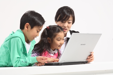 A female teacher and two kids looking at a laptop computer - isolated on whiteの写真素材