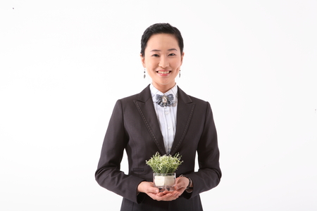 Asian businesswoman posing with a little potted plant - isolated on whiteの写真素材