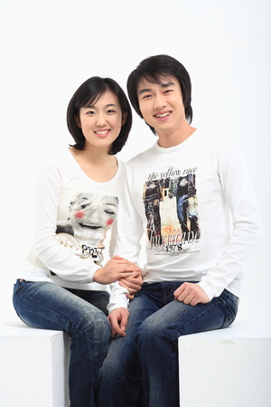 Young asian couple sitting in studio - isolated on whiteの写真素材