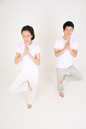 Young Asian couple doing yoga poses together - isolated on whiteの写真素材