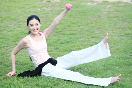 Young Asian woman working out with dumbbells in the parkの写真素材