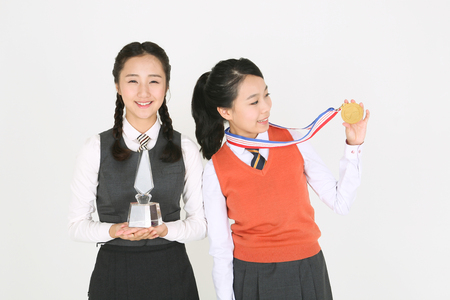 Asian girls in school uniform posing with trophy and gold medalの写真素材