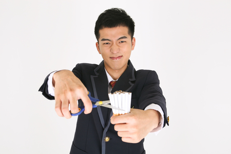 No smoking concept - Asian male student in school uniform cutting cigarettes with scissorsの写真素材