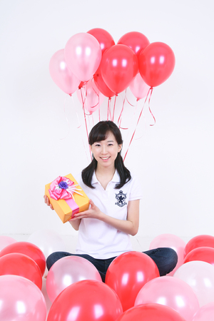 Party Concept - Young Asian woman showing a gift box with pink balloons, isolated on whiteのeditorial素材