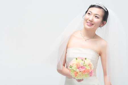 Beautiful Asian bride posing with bouquet, isolated on whiteの写真素材