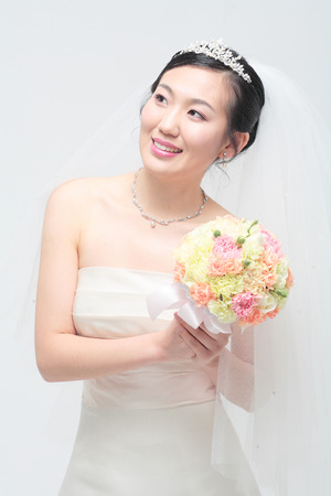 Beautiful Asian bride posing with bouquet, isolated on whiteの写真素材