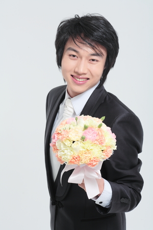 Happy Asian groom in tuxedo posing with bouquet in the studio - isolated on whiteの写真素材