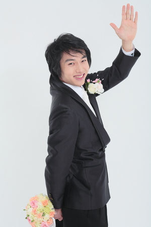 Happy Asian groom in tuxedo posing with bouquet in the studio - isolated on whiteの写真素材