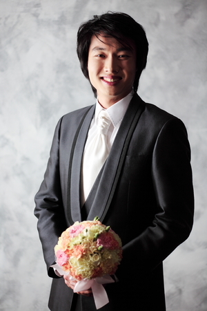 Happy Asian groom in tuxedo posing with bouquet in the studio - isolated on whiteの写真素材