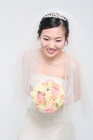 Beautiful Asian bride posing with bouquet, isolated on whiteの写真素材