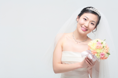 Beautiful Asian bride posing with bouquet, isolated on whiteの写真素材