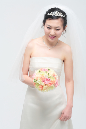 Beautiful Asian bride posing with bouquet, isolated on whiteの写真素材