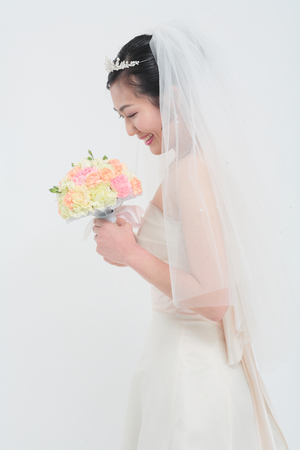 Beautiful Asian bride posing with bouquet, isolated on whiteの写真素材