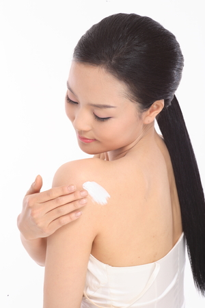 Beauty Concept - Beautiful Asian woman applying sunscreen on the back of her shoulder, isolated on whiteの写真素材