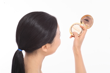 Beauty Concept - Beautiful Asian woman looking at mirror on compact pressed powder, isolated on whiteの写真素材